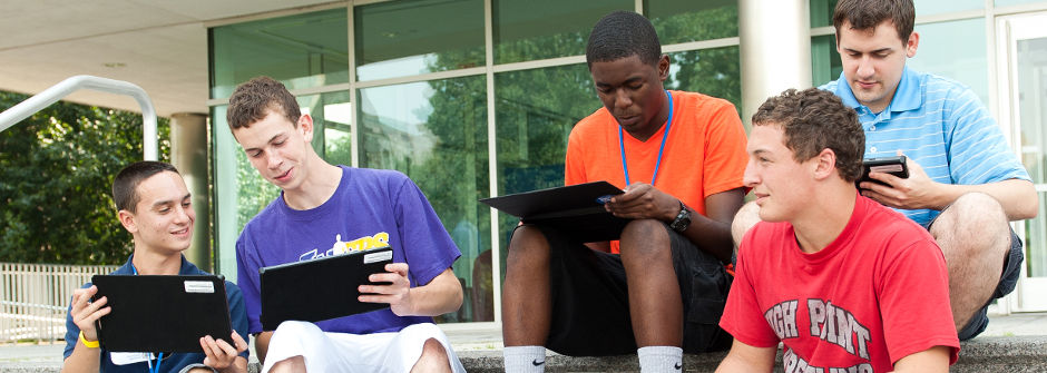 Students with technology sitting in front of Jubilee Hall. 