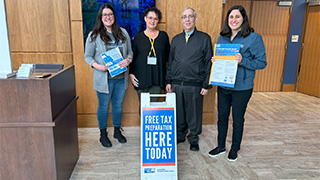 Four people at Seton Hall near a sign that says "Free Tax Preparation Here Today"