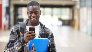 Student carrying books and texting on his phone. 