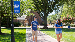 A male and female student walking on campus with masks.