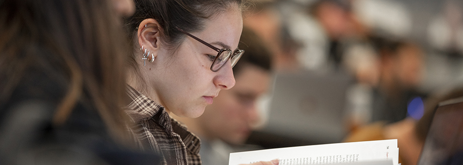 A person in a classroom with other students reading a book.