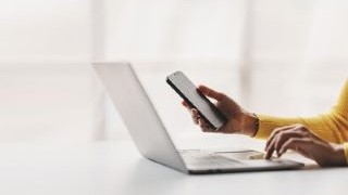 Woman on a laptop with a mobile phone in their hand.