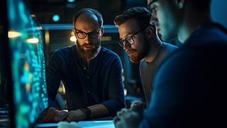 Three people working at a desktop and monitor.