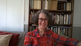Celia Deutsch wearing a red flannel, sitting in front of a bookcase