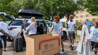 Image of volunteers, parents, and Sister Ann helping move bins out of a car during Move-In Day 2022. 