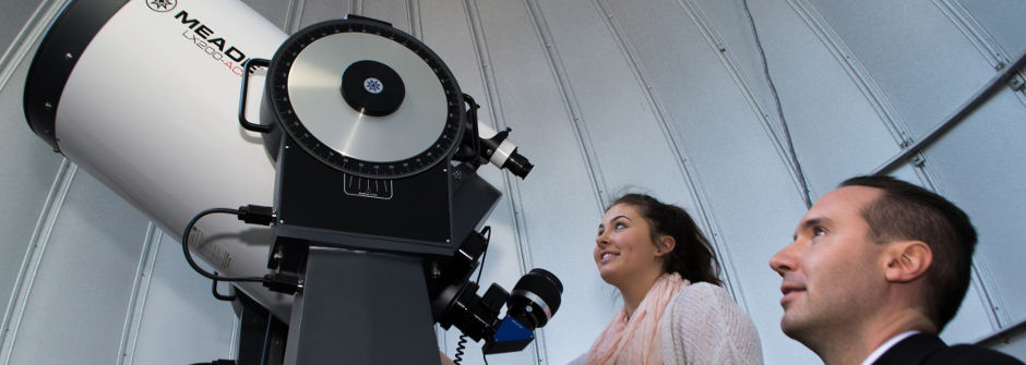 Student and Father Laracy looking through a telescope in the observatory. 