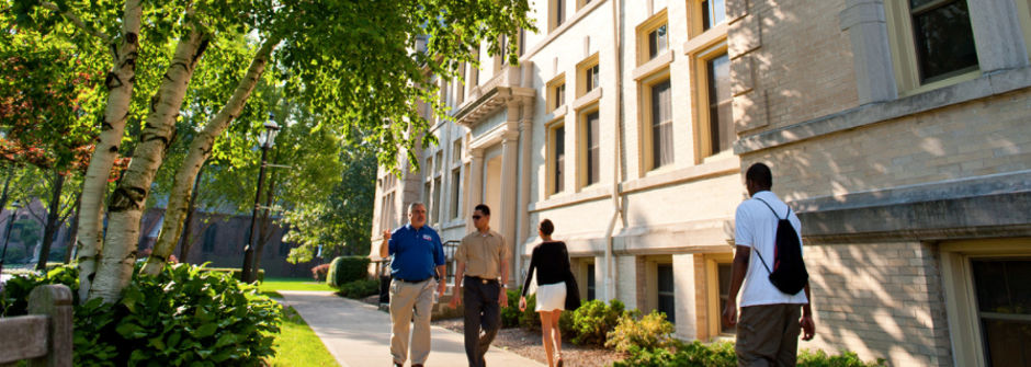 Image of students and workers walking along a path on campus in the spring. 