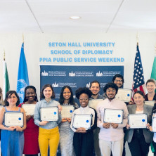 Diplomacy students standing in front of flags at the PPIA Public Service Weekend. The students are each holding certificates of completion of the program.