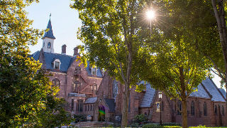 Side view of President's Hall and the Chapel with sun shining through trees. 